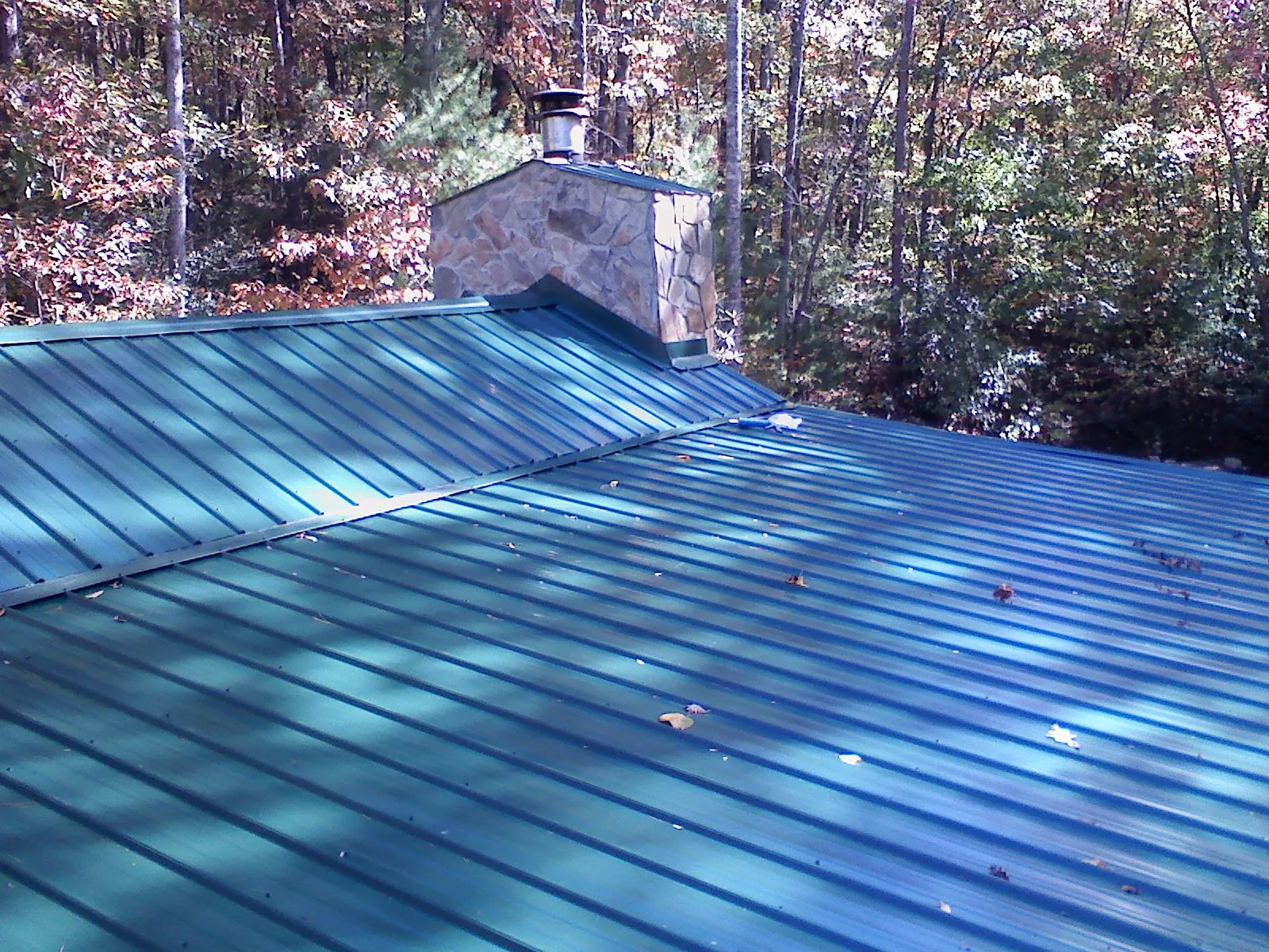 New green metal roof and stone chimney surrounded by autumn woods in Avon